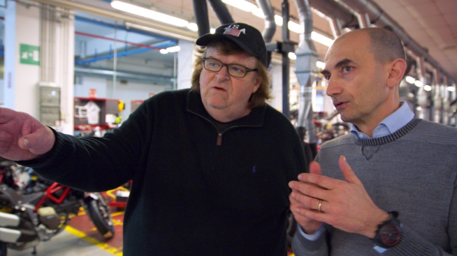 This image provided by Dog Eat Dog Films shows director Michael Moore, left,  and Claudio Domenicali, CEO of Ducati, in a scene from his documentary, "Where to Invade Next." The movie opens in U.S. theaters on Feb. 12, 2016. (Dog Eat Dog Films via AP)