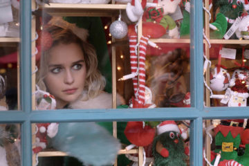 Emilia Clarke looks through a window of the Christmas shop in LAST CHRISTMAS (2019).