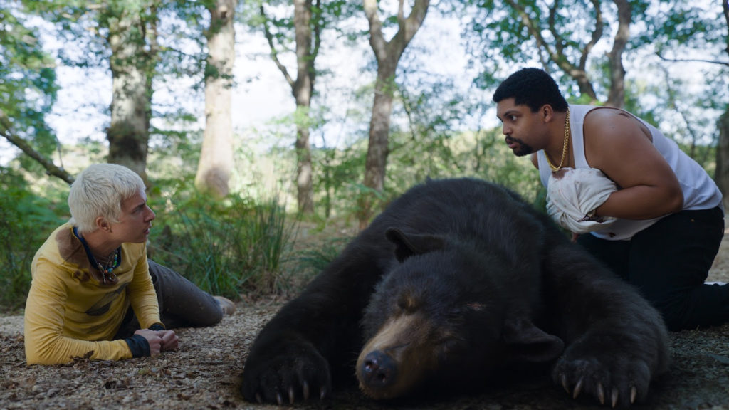 Aaron Holliday and O'Shea Jackson Jr. whisper around the sleeping COCAINE BEAR (2023)